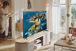 Foto colorida de uma Smart TV Samsung CU7700 em cima de um rack bege em uma sala de estar